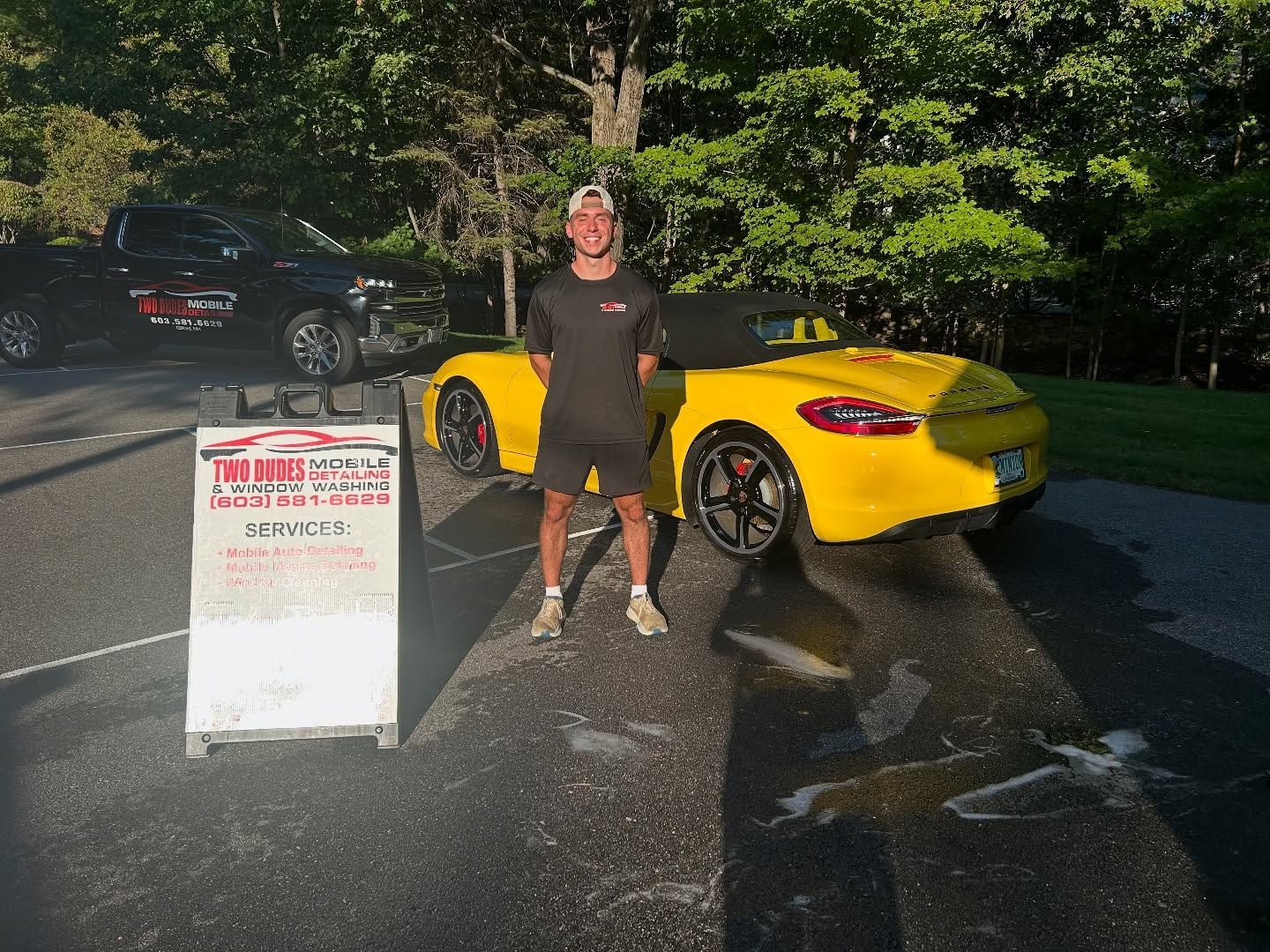 Person standing beside a yellow sports car and a sign on a wet parking lot at night