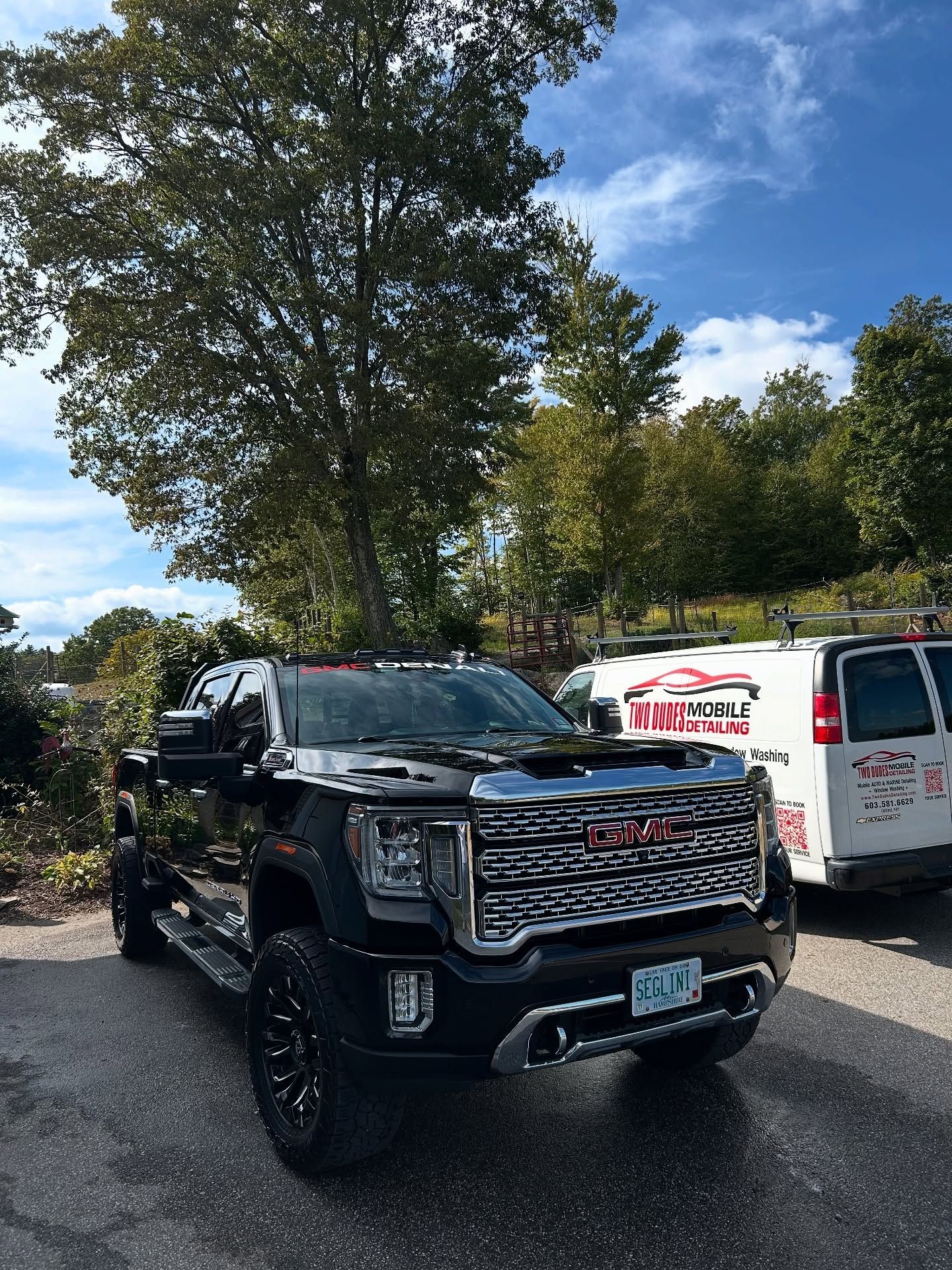 Black GMC pickup truck parked on a tree-lined street under a blue sky