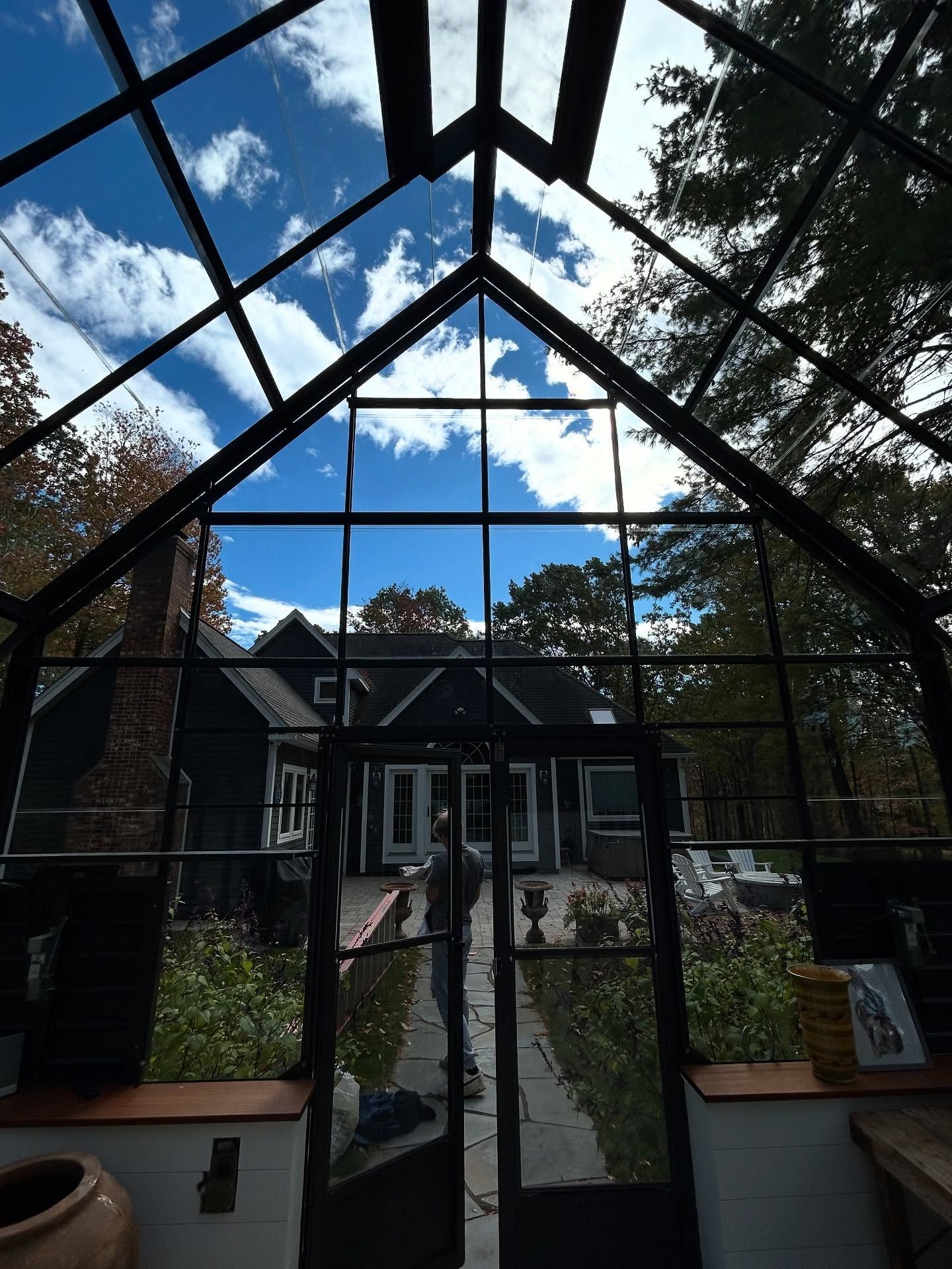 Glass-roof conservatory doorway opening to a garden path and house under a blue sky with clouds
