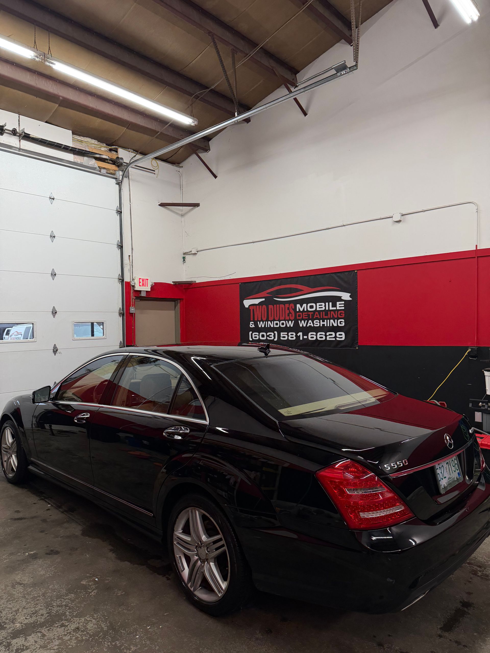 Black sedan in a garage with red and white walls and a banner on the back wall.