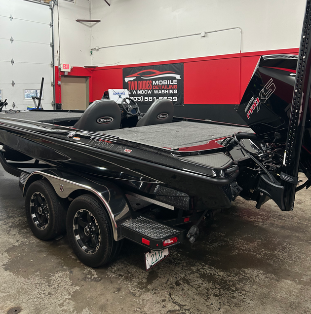 Black bass boat on a trailer in a wet indoor garage, with red wall and large trolling motor.