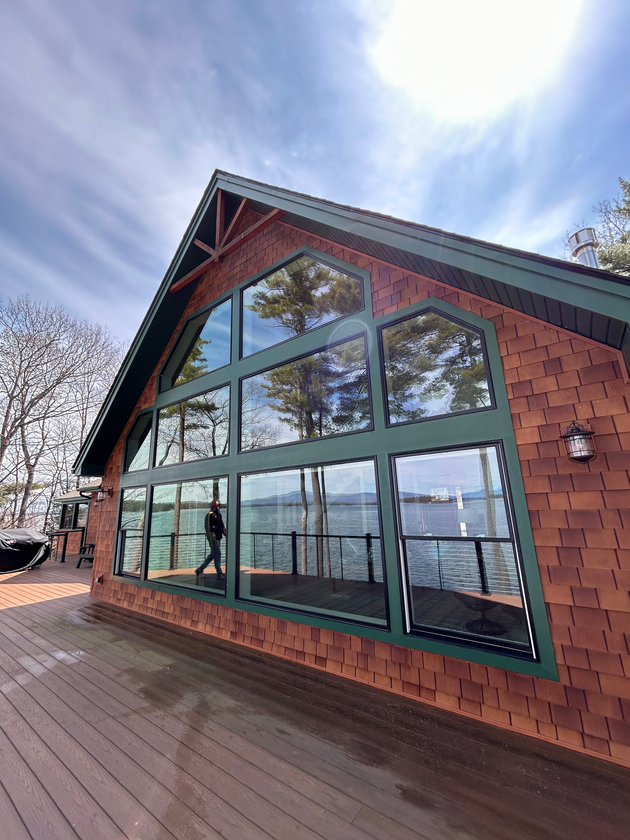 Modern cabin-style building with large windows, red shingle siding, and a sloped roof on a sunny day