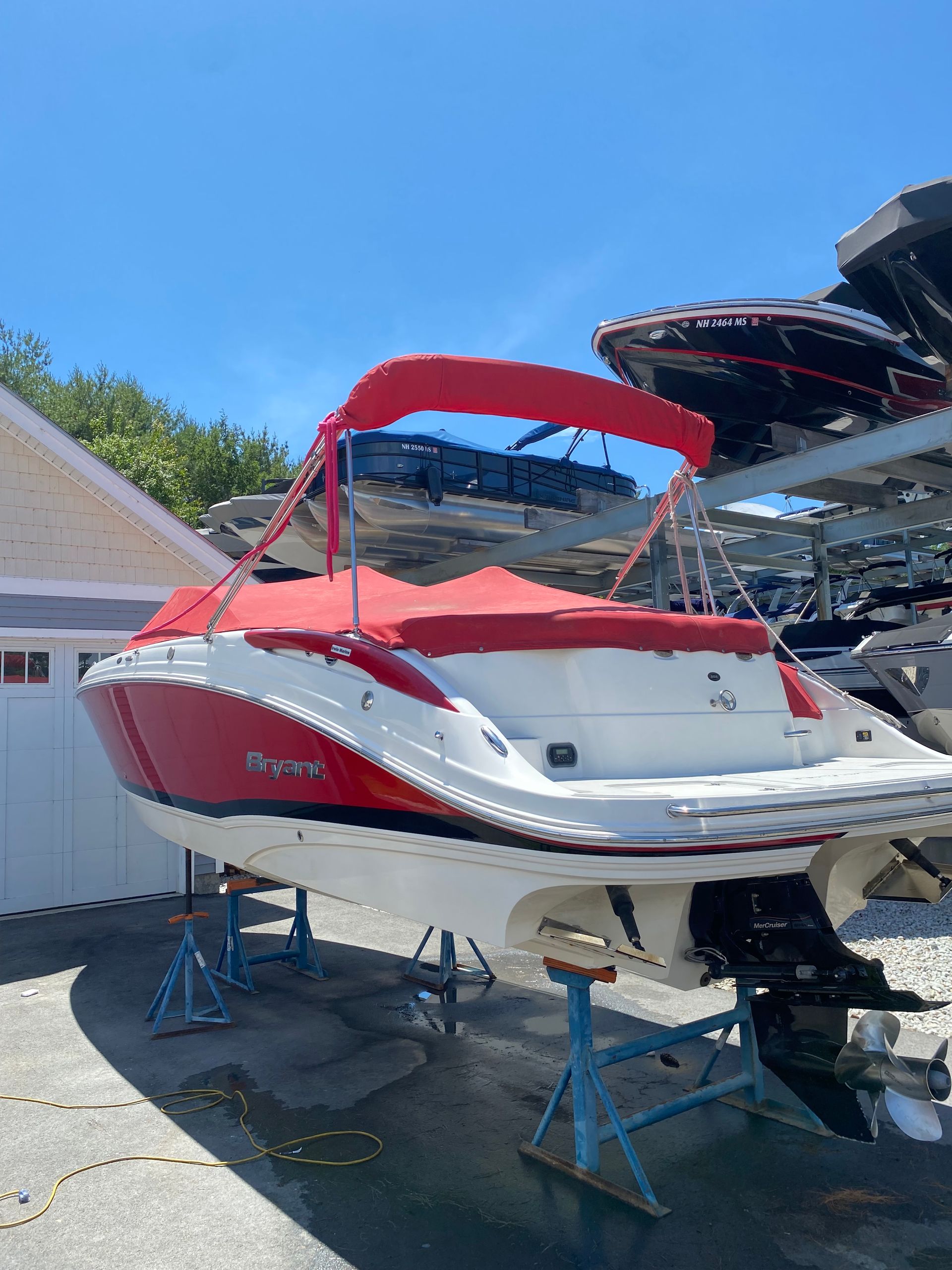 Red and white speedboat on blue stands in a driveway under a bright blue sky, with a red canopy.