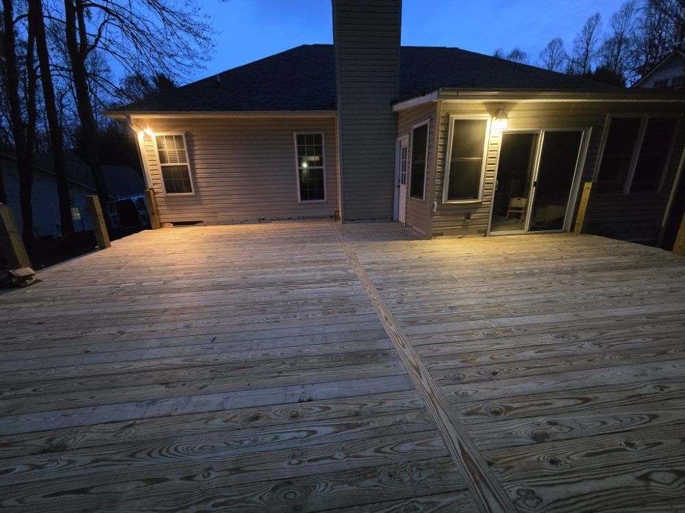 Wooden deck lit by warm lights, extending from a house at dusk.