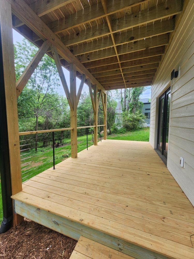 Wooden deck with black railings and covered ceiling, next to a house with sliding glass doors.