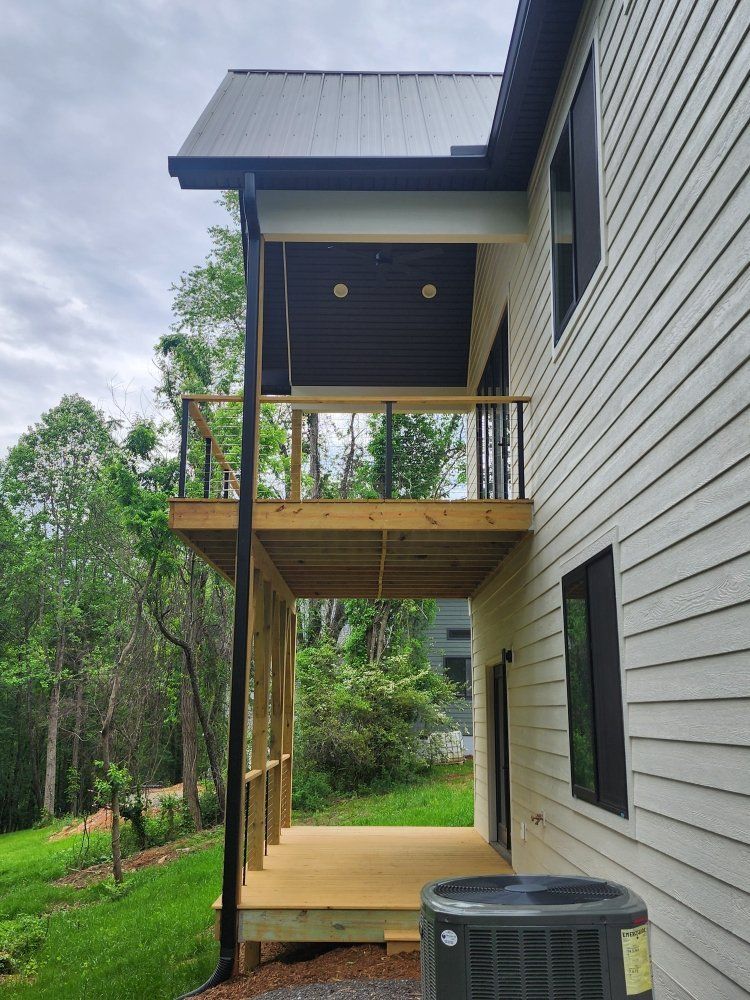Two-story wooden deck attached to a house with gray siding; black railings, a black gutter, and a gray AC unit.