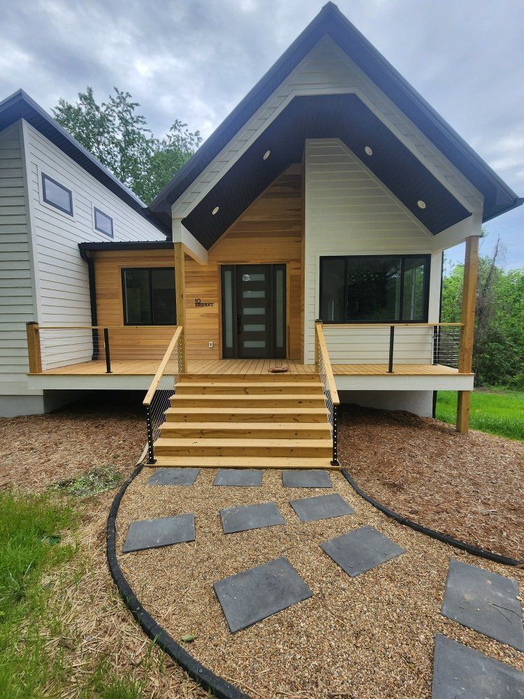 Modern house with wood and white siding, stairs, and stone walkway.