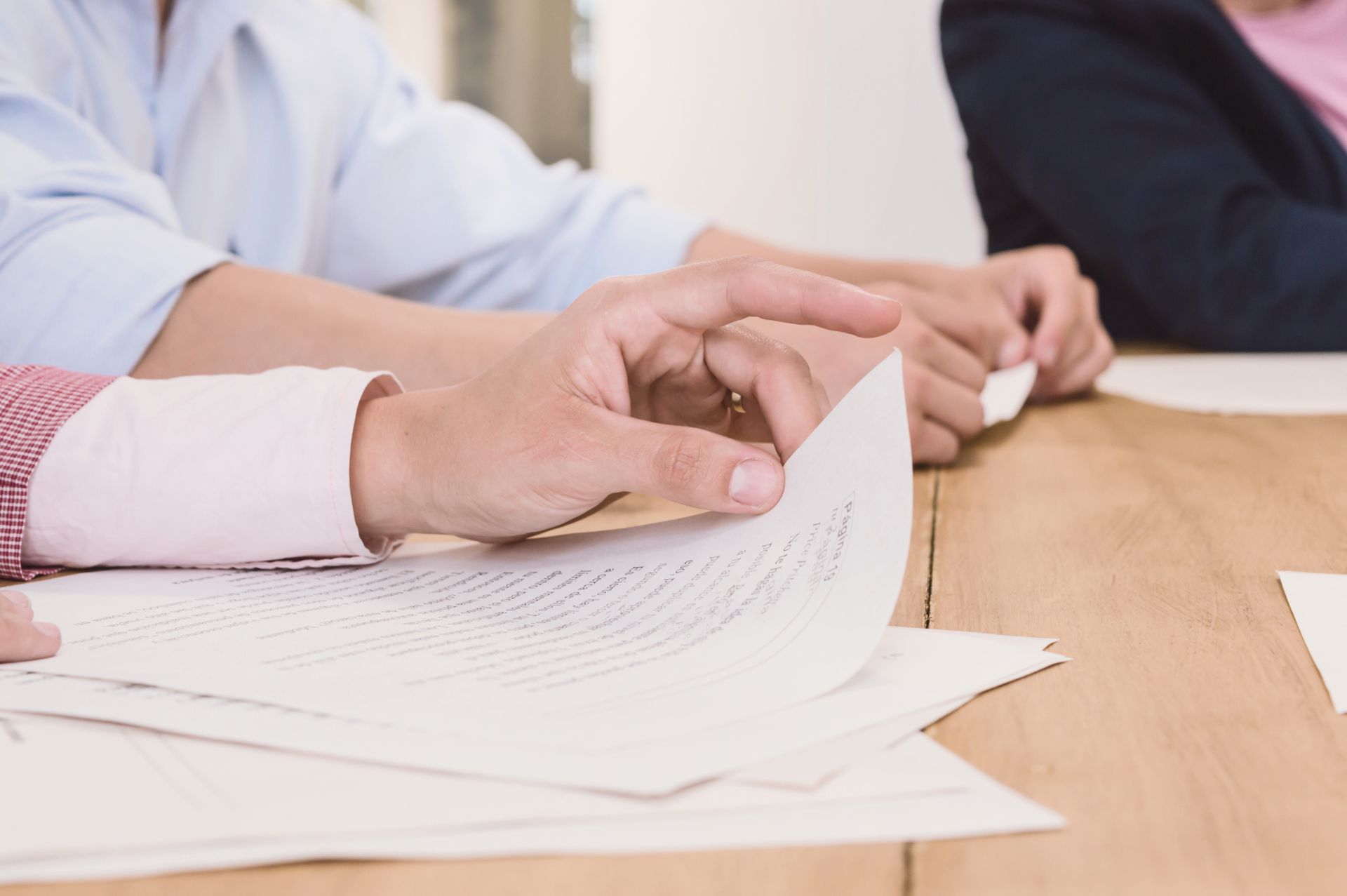 Hands of people at a table, turning pages of a document during a meeting.