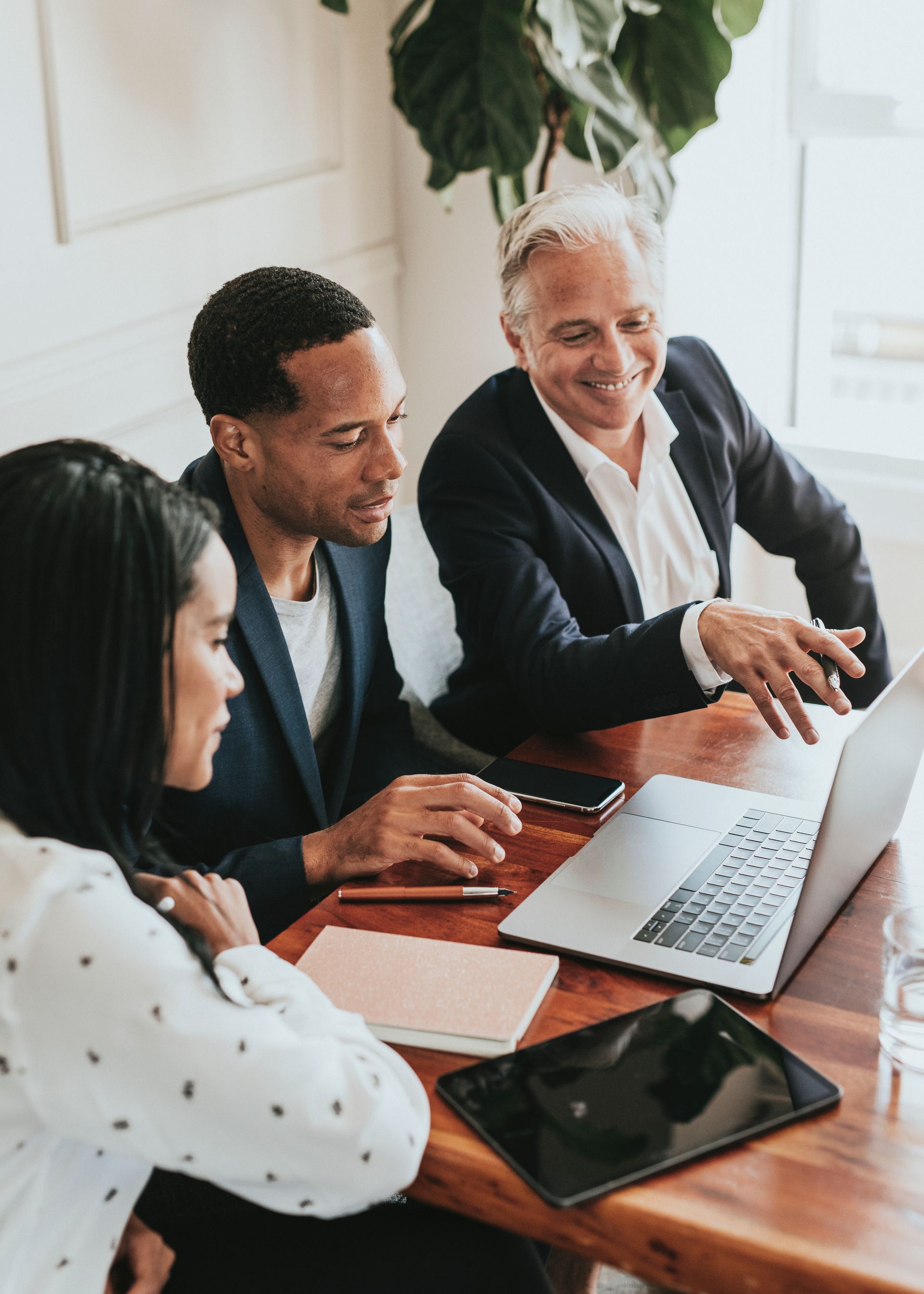 Three people looking at laptop screen in a bright office, one pointing at the screen.