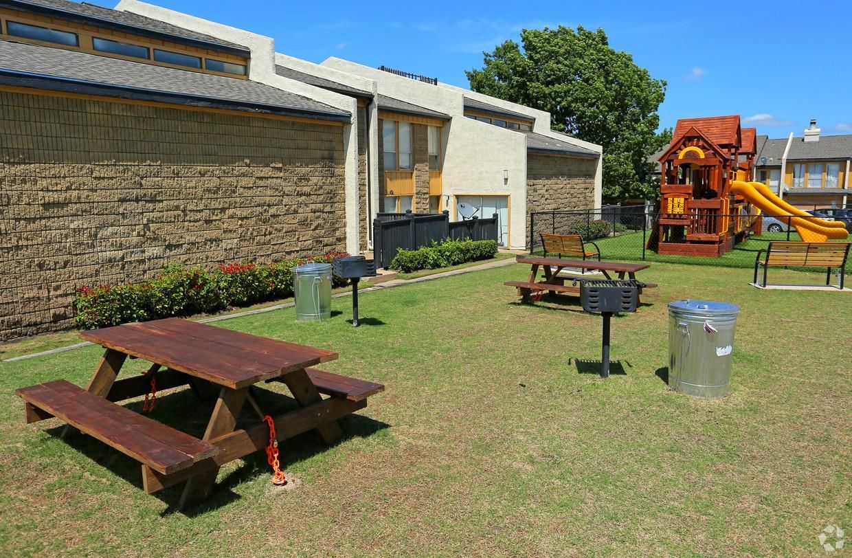 A picnic table is sitting in the grass in front of a playground.