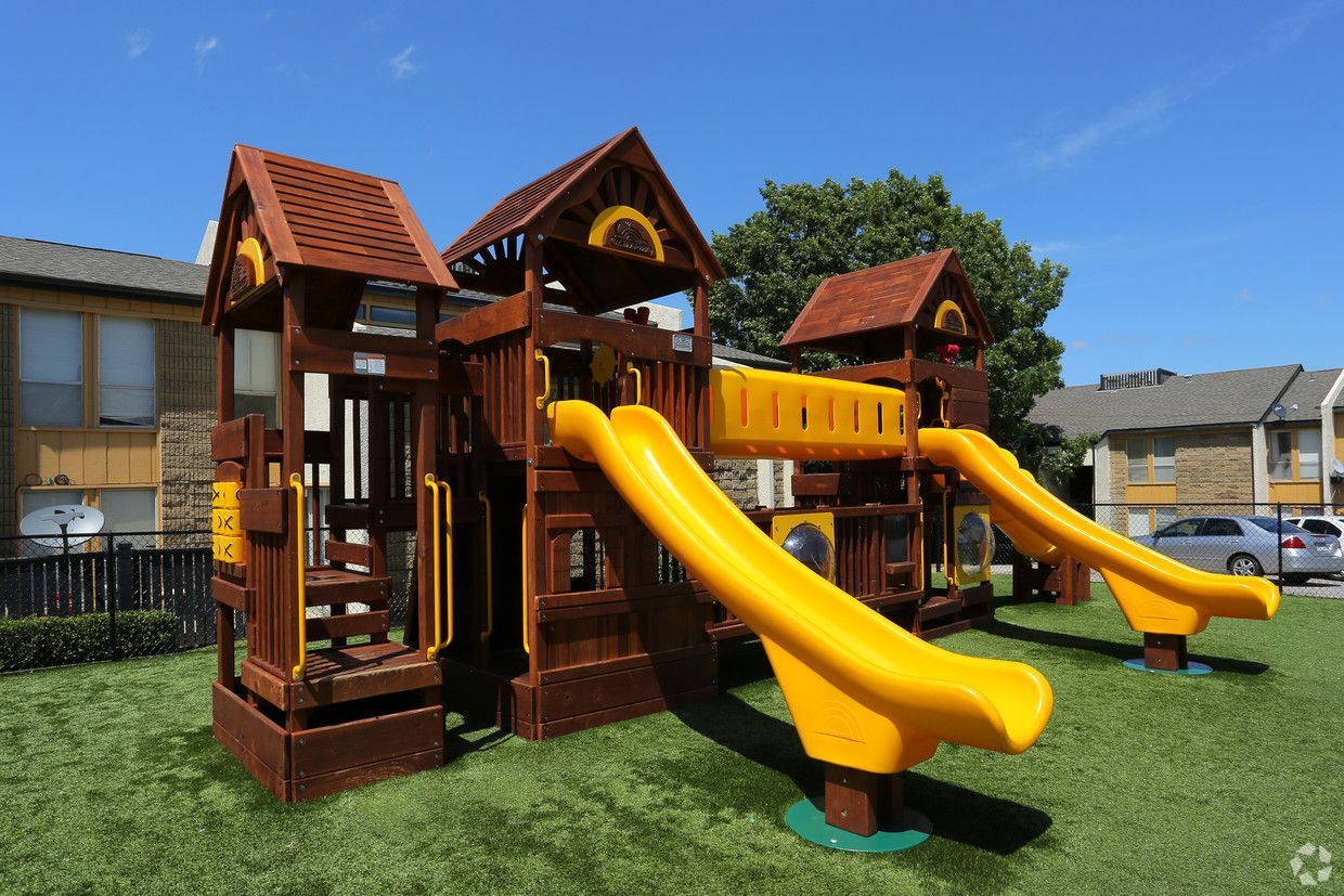 A wooden playground with yellow slides and stairs in front of a building.