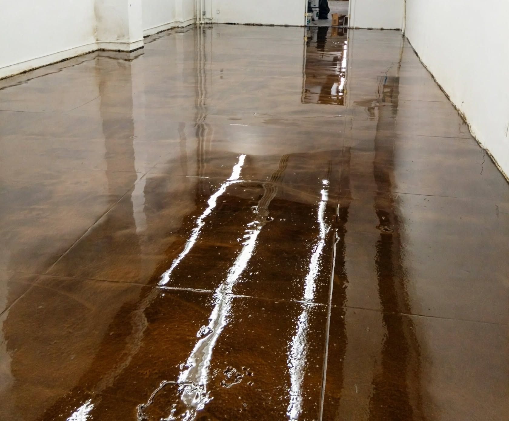Two people walk in a shiny empty hallway with white walls and a black floor