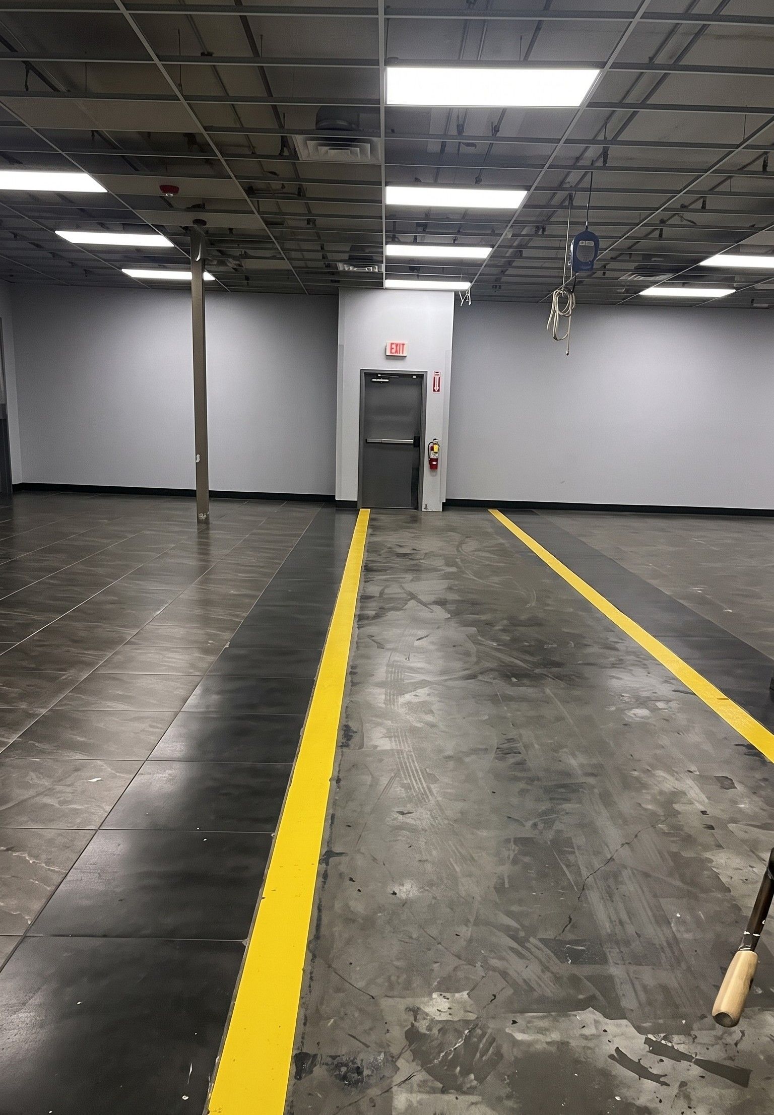 Empty warehouse interior with gray floor, yellow aisle lines, and a door on the back wall