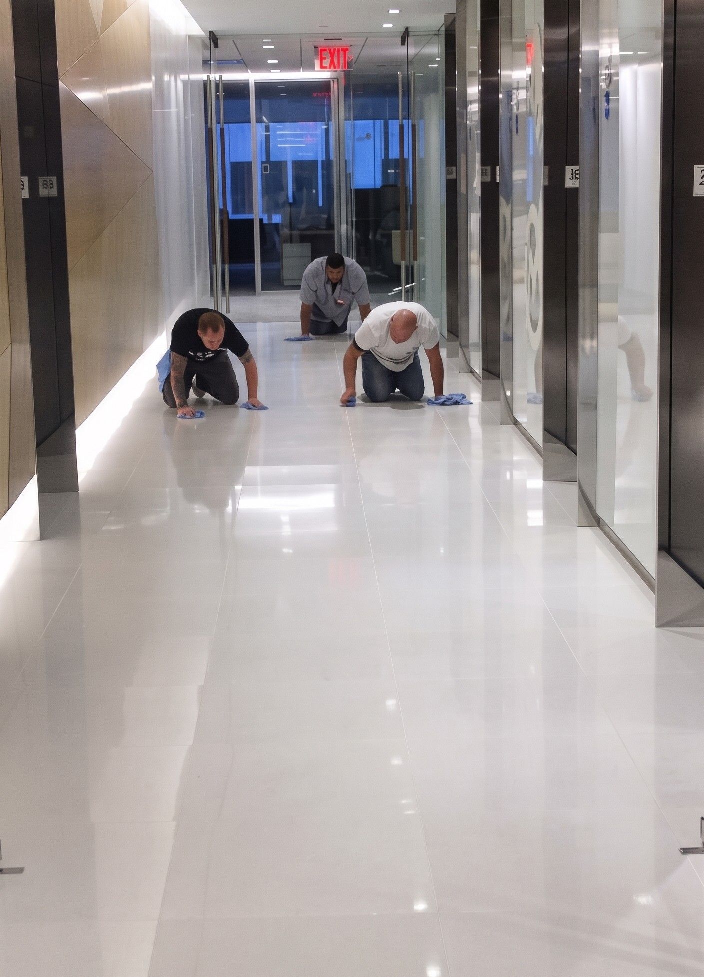 Three people crawling down a shiny hallway in a building corridor