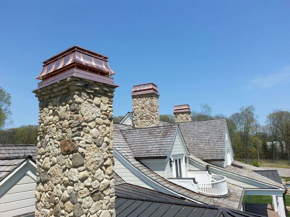 Stone chimneys and gray shingle roof on a house under a clear blue sky