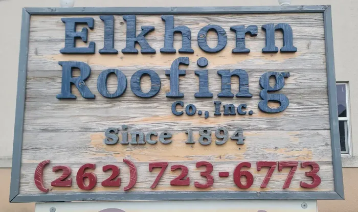 Elkhorn Roofing Co., Inc. sign on a weathered gray board with blue and red lettering and phone number