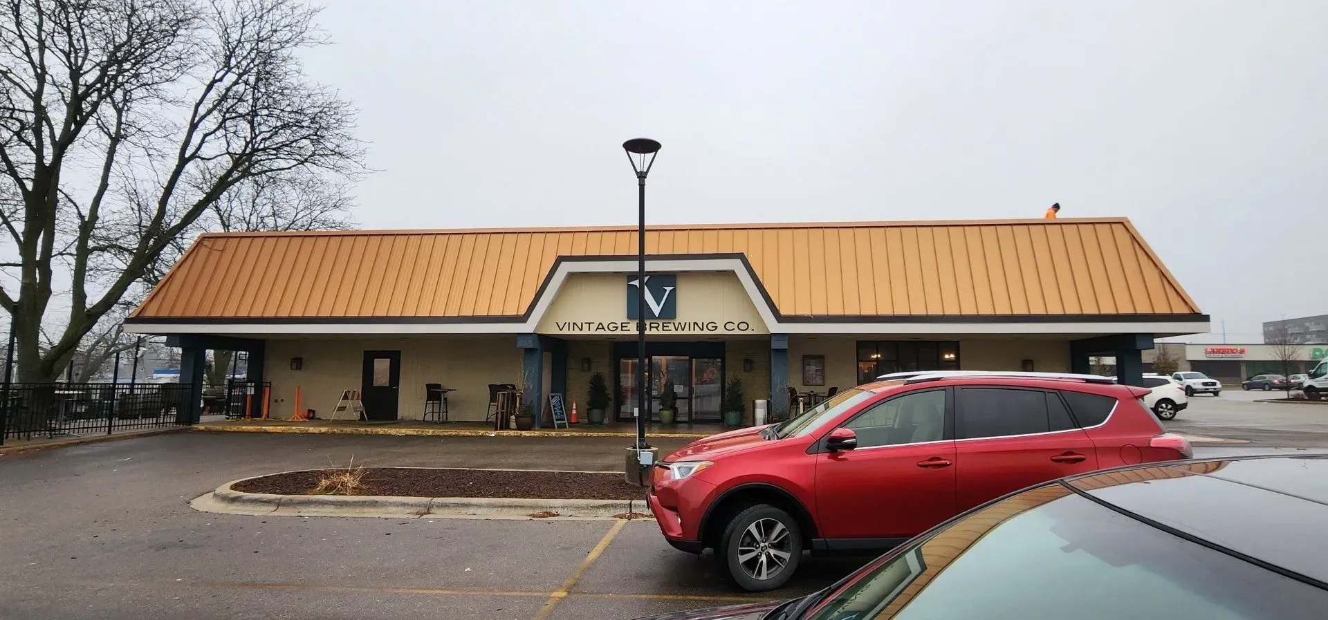 Exterior view of a building with a red car parked in front. Cloudy day, parking lot. Drive-thru restaurant with orange roof and a red SUV in front on a cloudy day