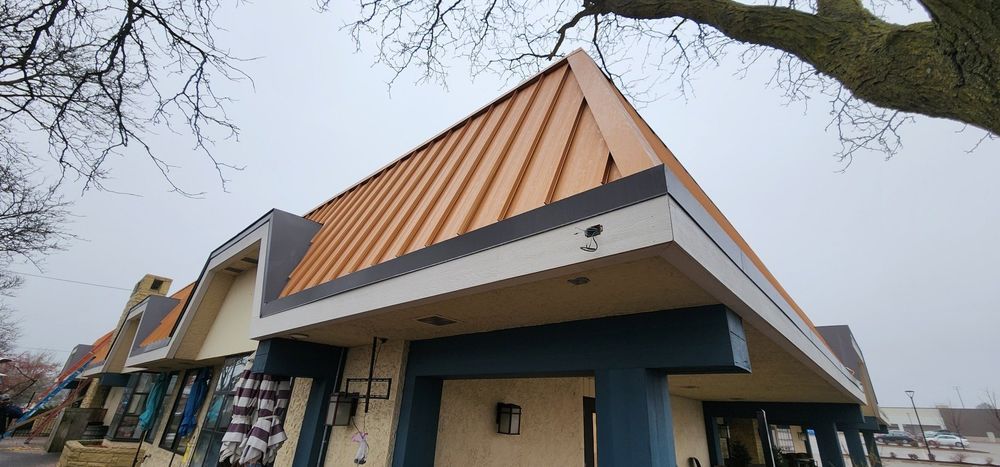 Low-angle view of a building with a copper-colored sloped roof and storefronts on a cloudy day