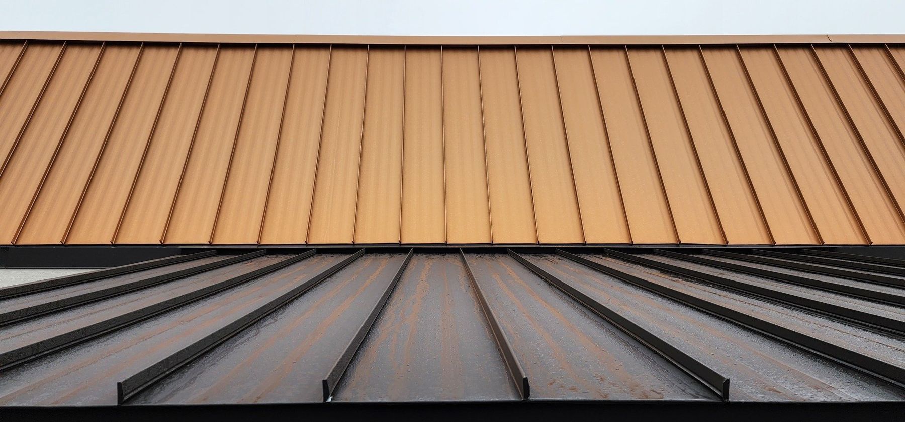 Two metal roof sections meeting at a seam, one tan and one gray.