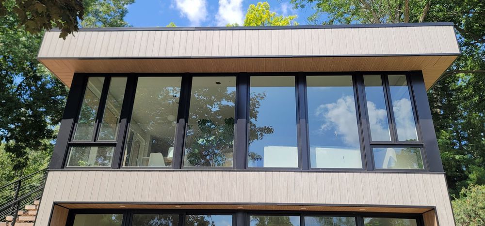 Modern house facade with large reflective windows and a flat roof under trees
