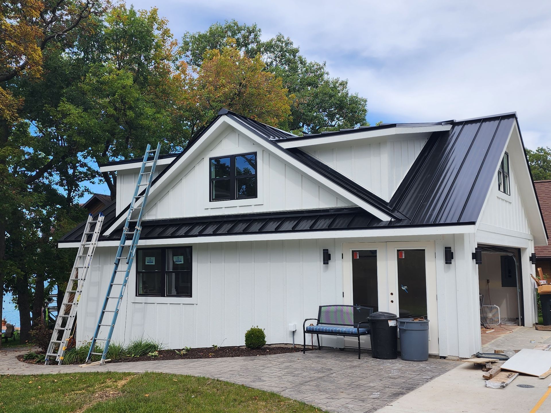 House under renovation with workers’ ladder, black roof, and white siding