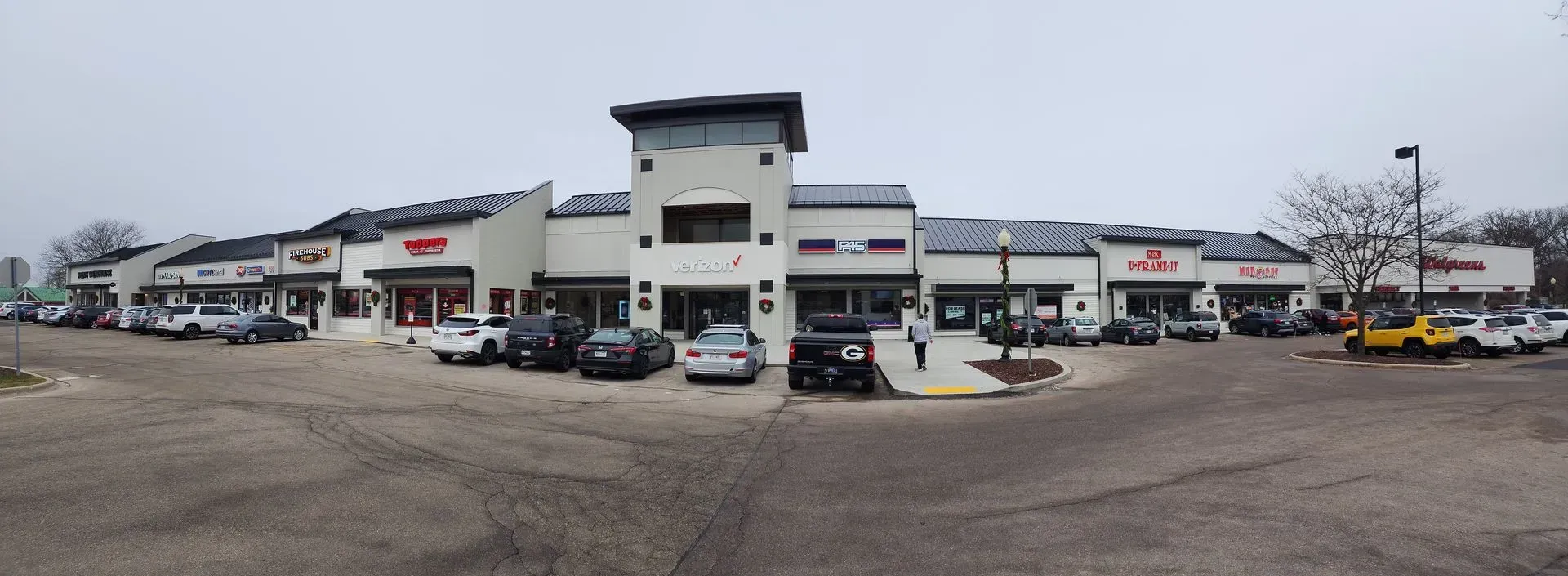 Shops in a strip mall, parked cars, gray overcast sky. Wide shopping center strip mall with parked cars on an overcast day