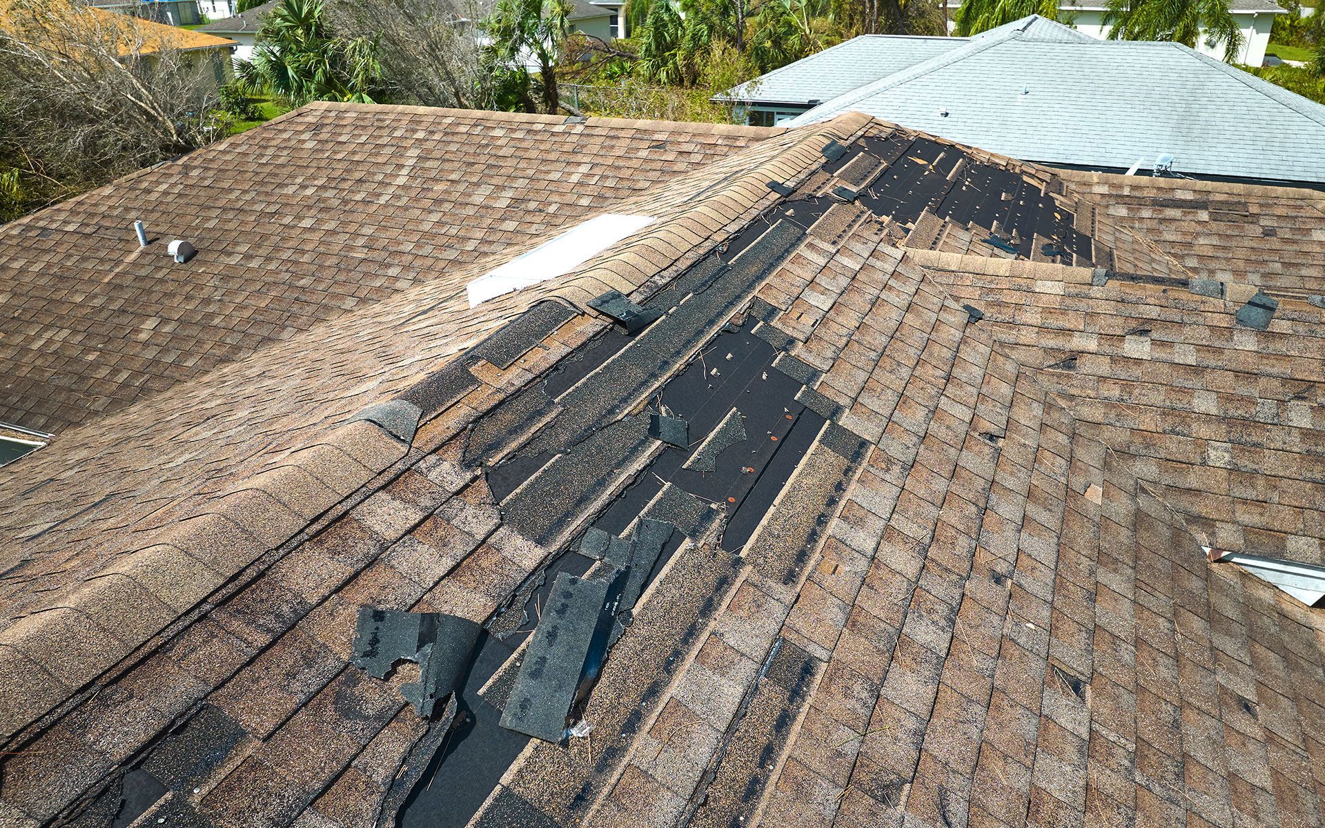 Damaged asphalt shingle roof with missing and torn shingles, sunlight.