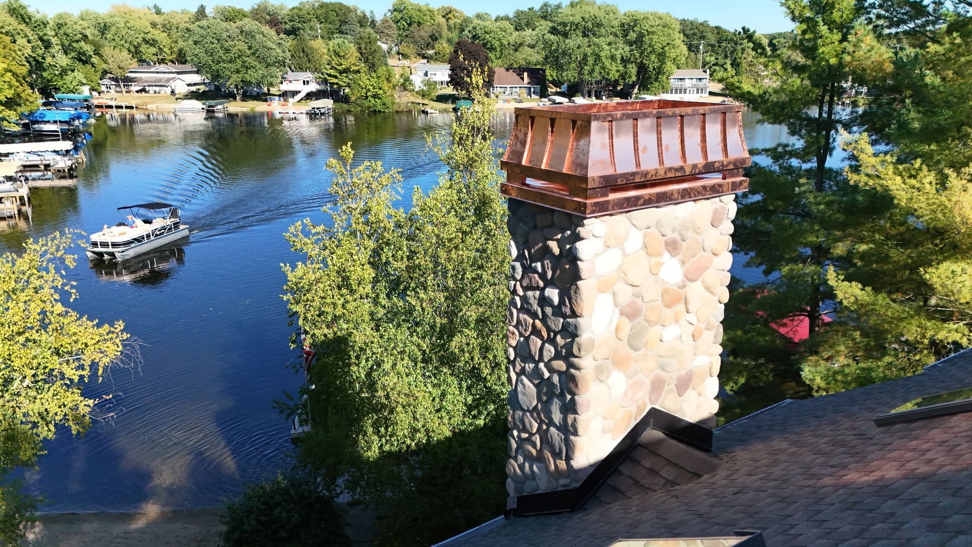 A river with a white boat, trees along the shore, and a stone chimney in the foreground.