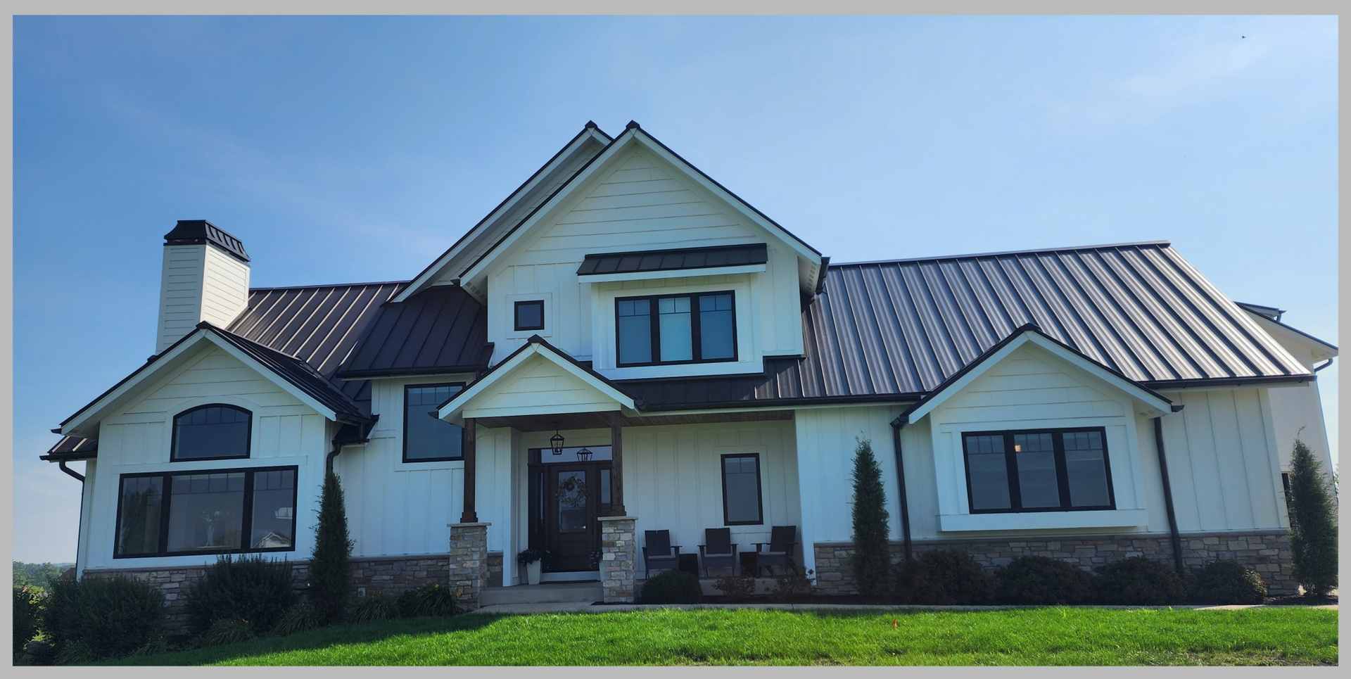 White two-story house with gabled roof, central front porch, and stone trim under a clear blue sky