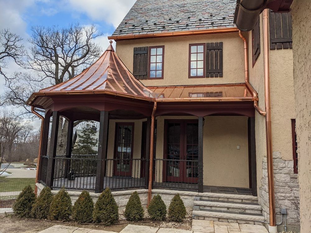 Historic house with copper-roofed porch, beige walls, and stone steps under a cloudy sky