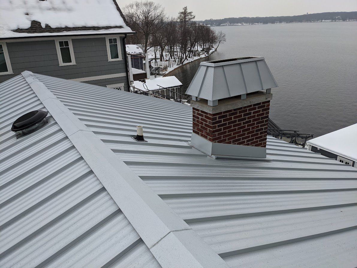 Snow-covered metal roof with a brick chimney beside a frozen waterfront