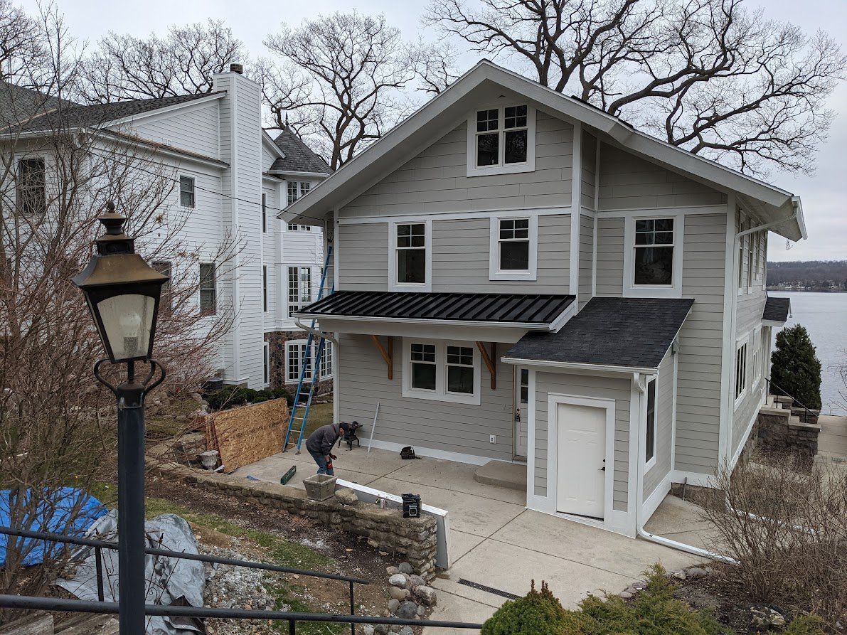 Gray two-story house with white trim and a small porch on a wooded hillside
