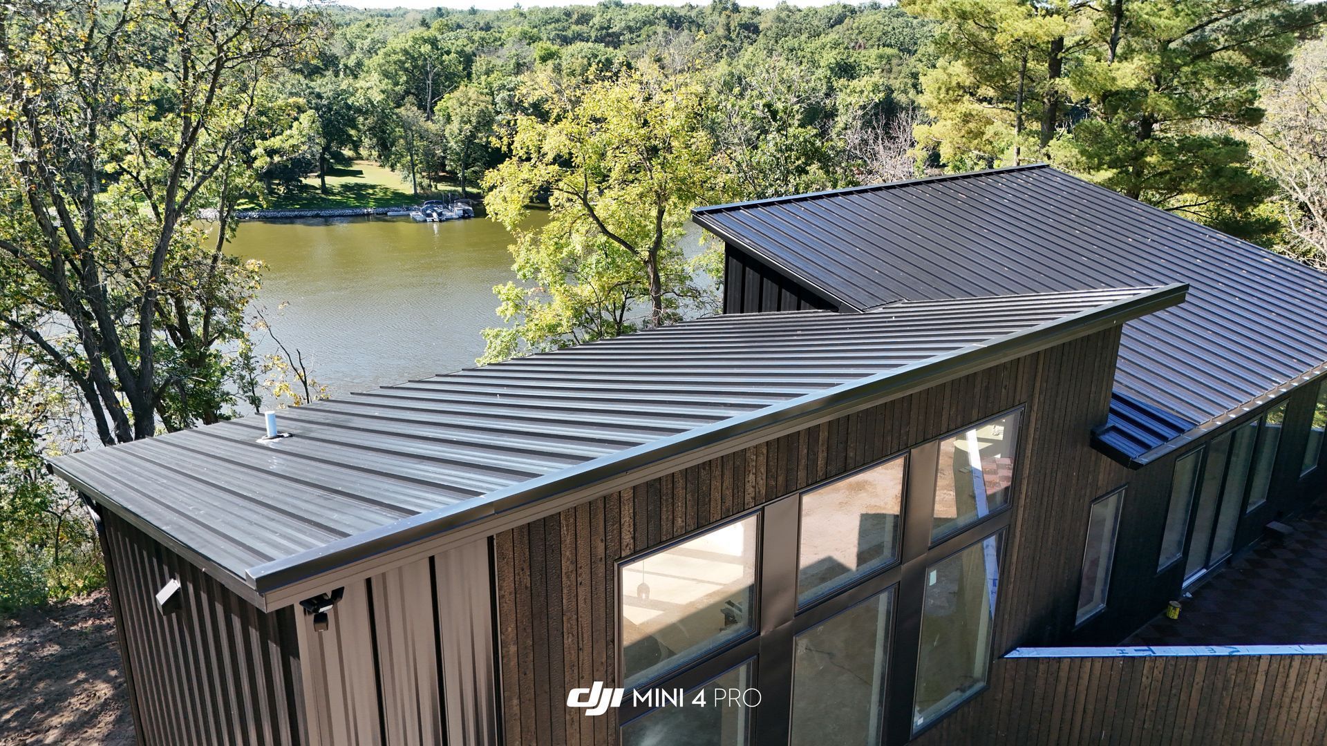 Modern cabin with dark metal roof overlooking a lake and trees