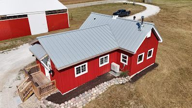 Red farmhouse with gray roof and white trim beside a barn on a rural property