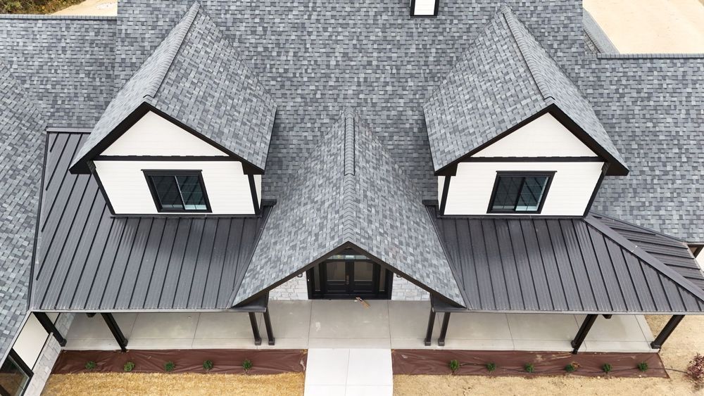 Aerial view of a gray shingled house roof with dormer windows and a front porch.