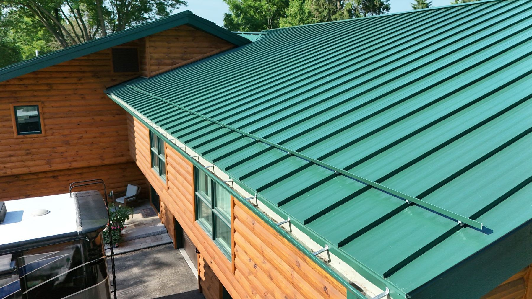 Green metal roof on a wooden cabin with skylights, viewed from above beside trees