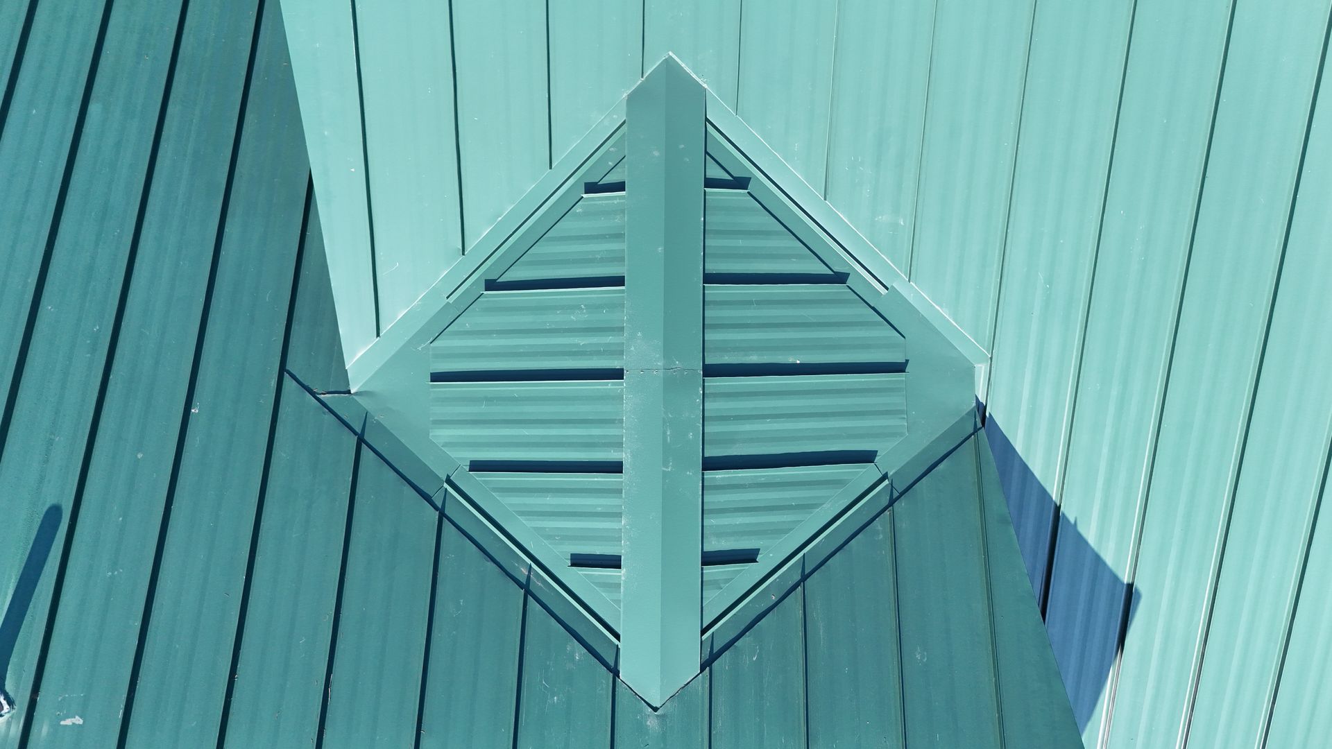 Teal wooden siding with a centered diamond-shaped vent or decorative panel