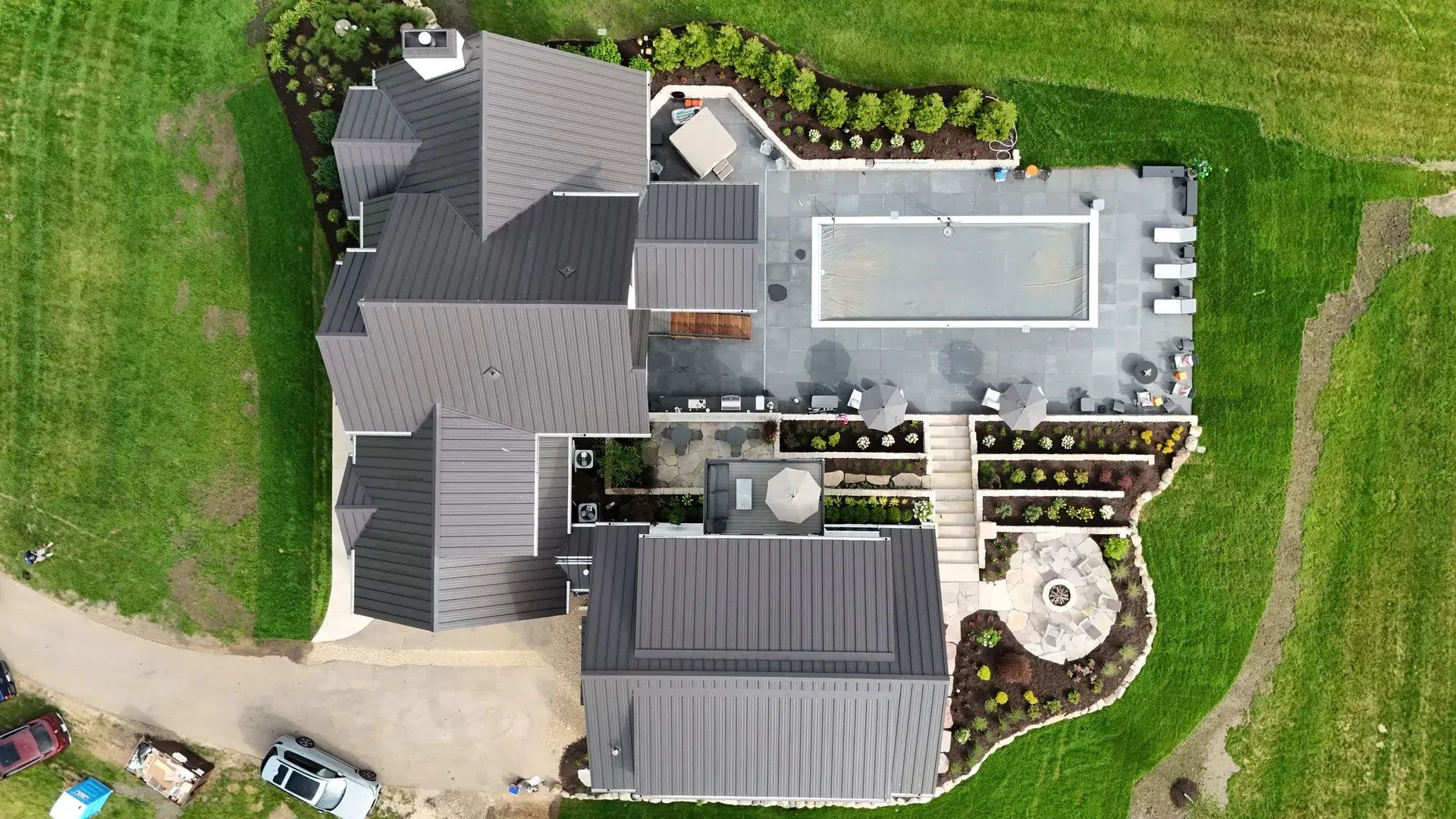 Aerial view of a modern home with a pool, patio, fire pit, and surrounding greenery. Aerial view of a large house with a pool, patio, and surrounding green lawn.