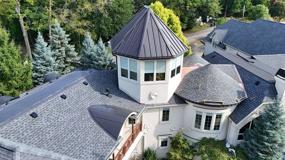 Aerial view of a large house with gray roofs and a central turret surrounded by trees