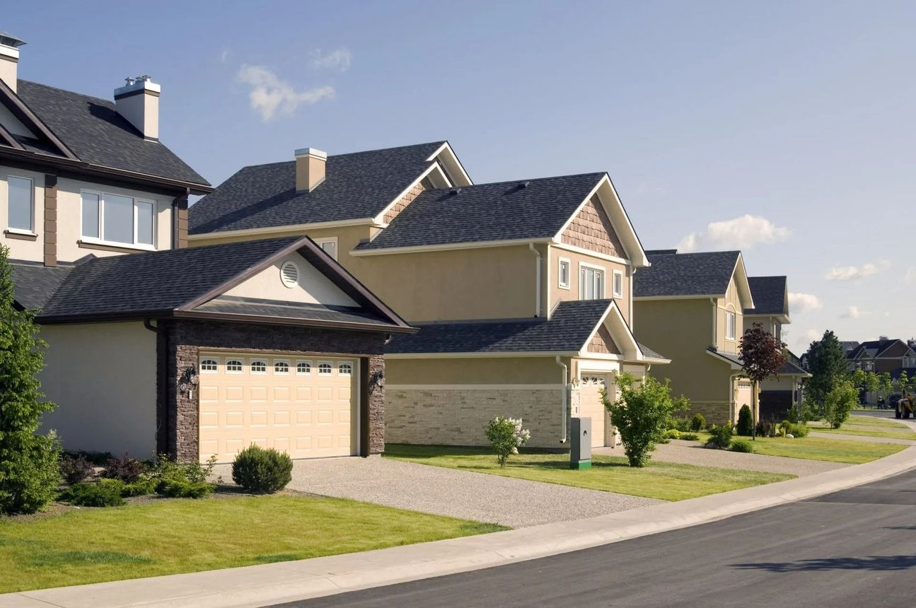 Suburban street with modern beige houses, garages, and a curved road under a clear sky