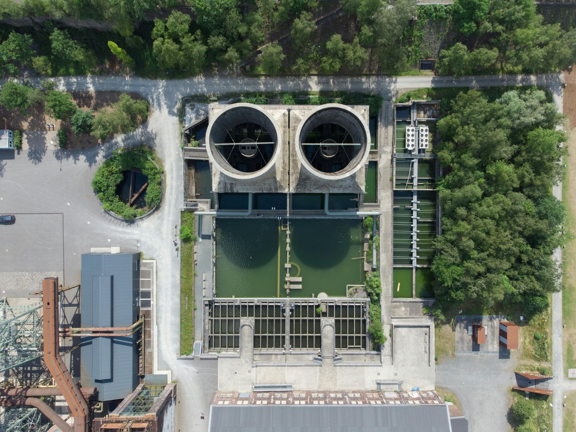 Overhead view of an industrial water treatment plant with two cooling towers, surrounded by trees and pathways.