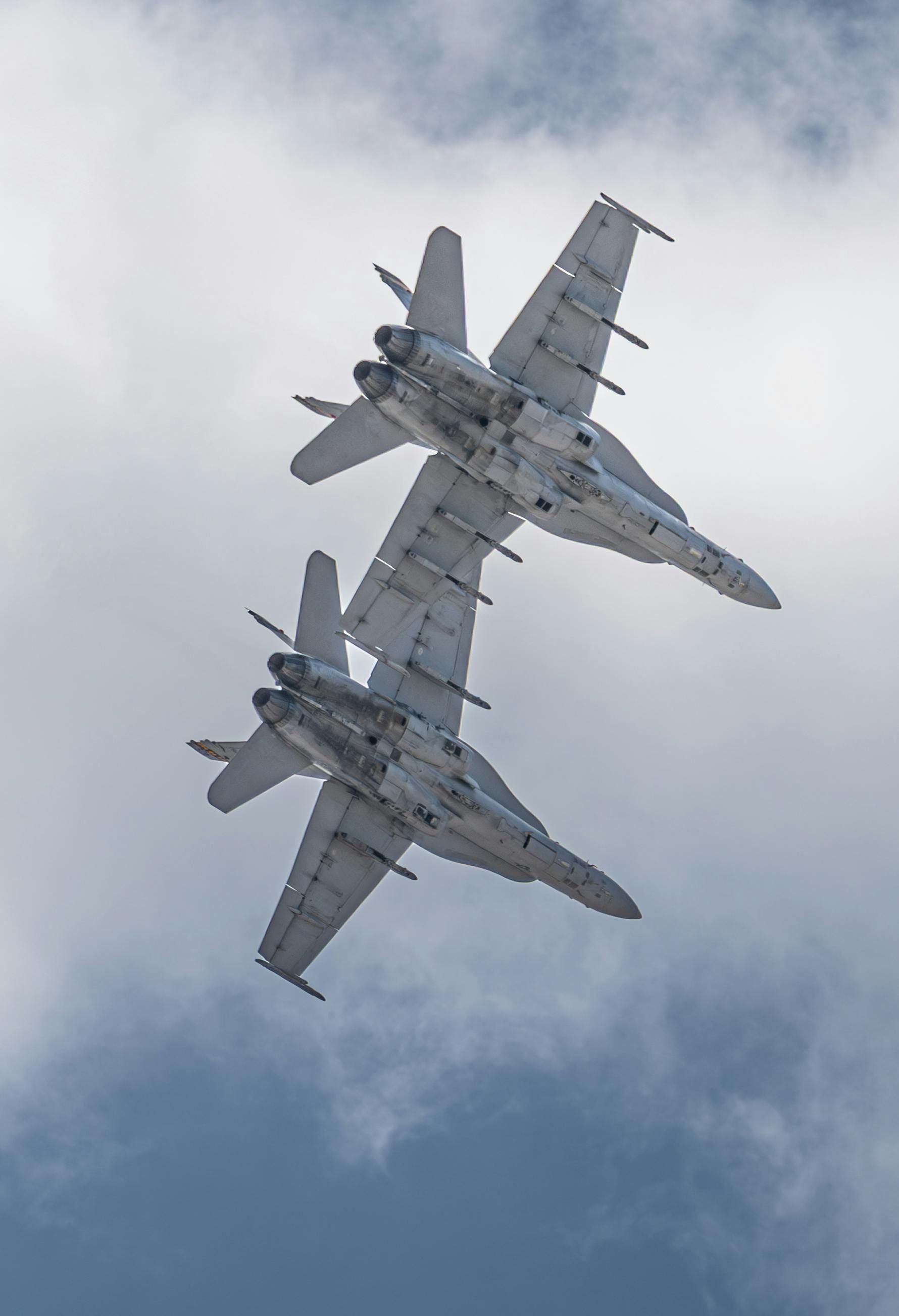 Two gray fighter jets in formation, against a cloudy sky.