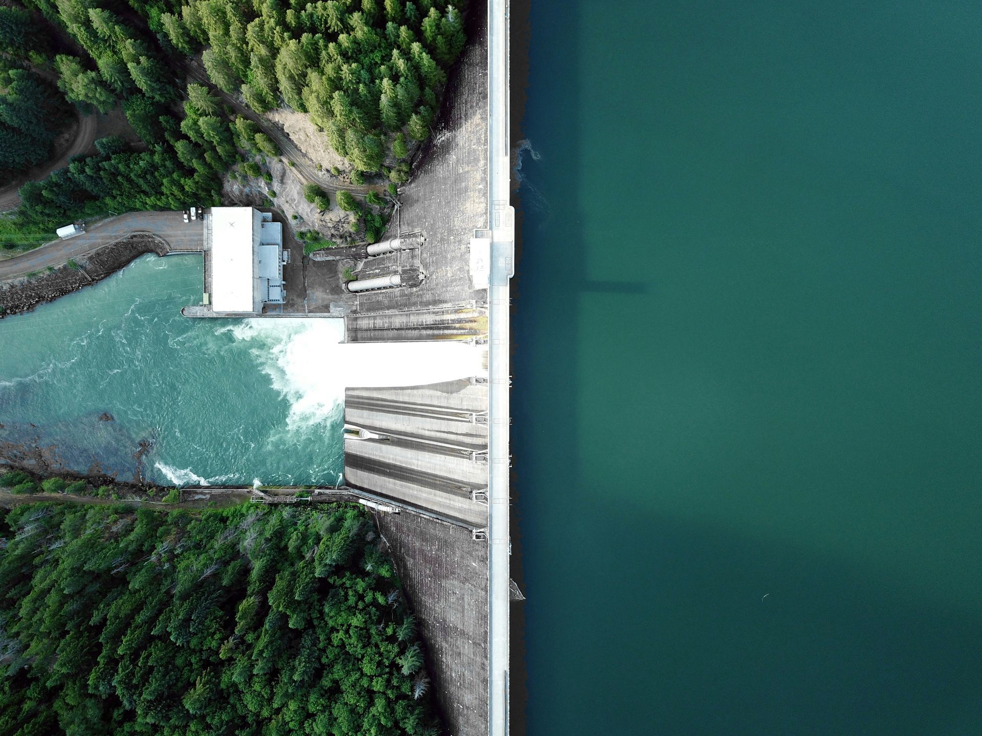 Aerial view of a building next to a road and forest, adjacent to a body of water.