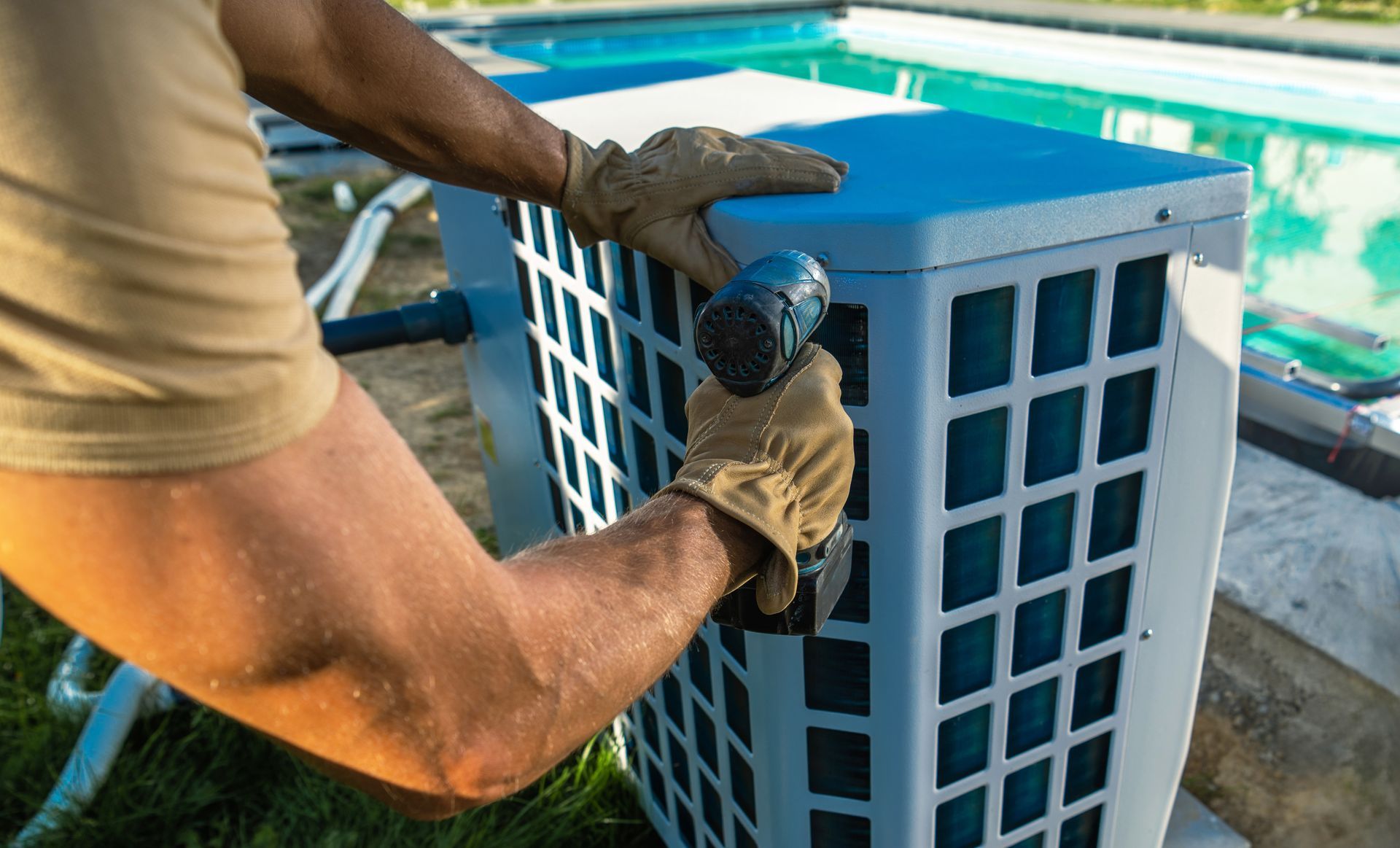 Person in work gloves using a tool on a blue pool heater near a pool.