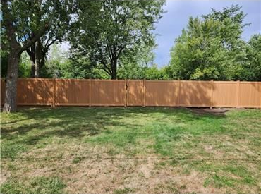 Fence installation contractor built wood privacy fence along a tree-lined backyard lawn.
