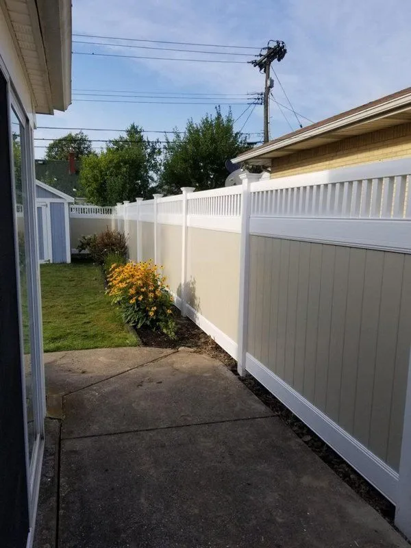 Beige and white fence lines yard with flowers and shrubs