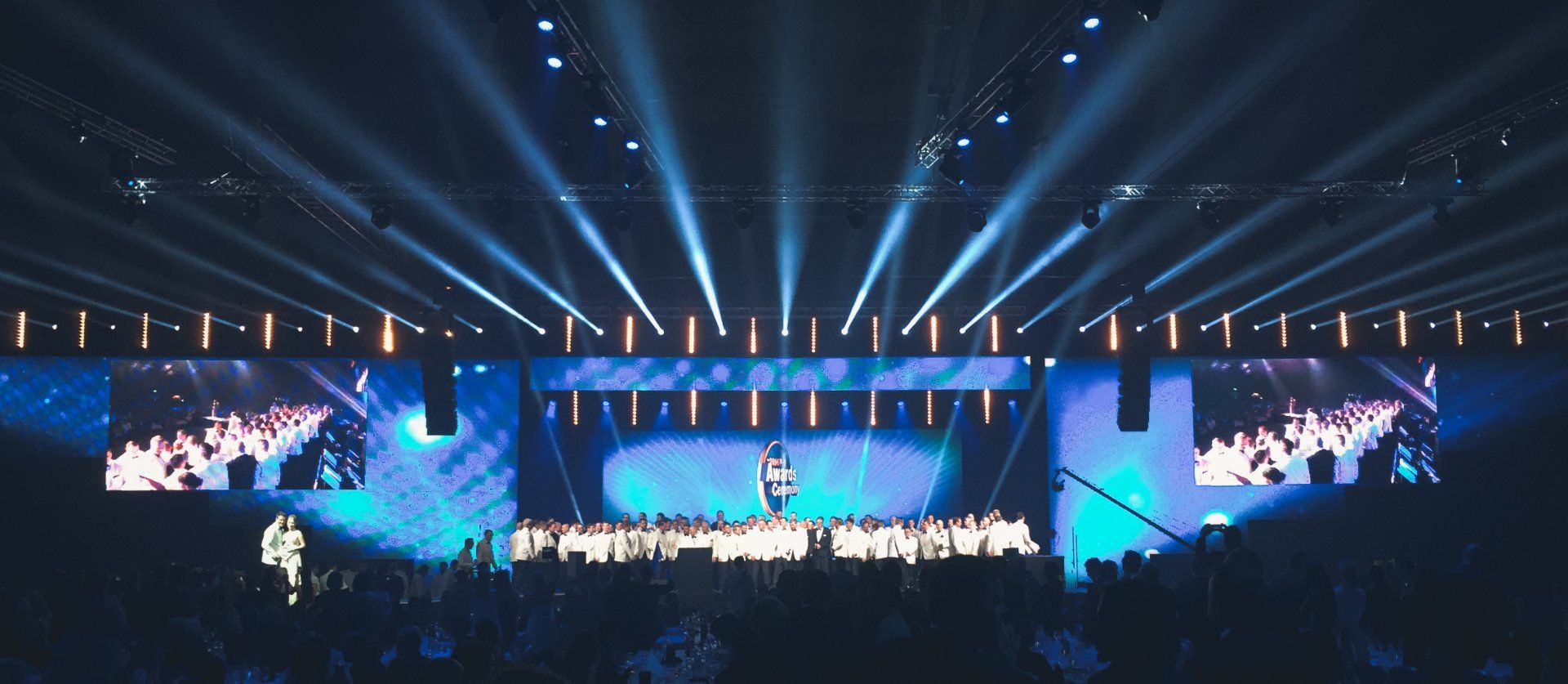 Konserttilava, jossa on kirkkaansinisiä valoja, esiintyjiä ja suuria näyttöjä. Yleisö näkyy etualalla.