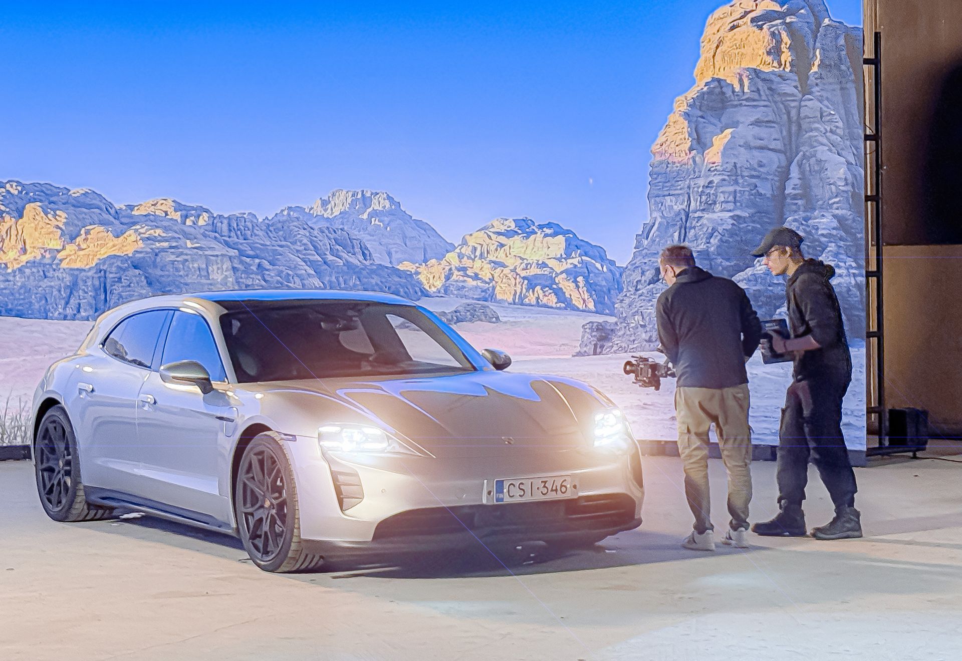 Hopeinen Porsche Taycan Cross Turismo ja kaksi miestä sen vieressä aavikkotaustan edessä.