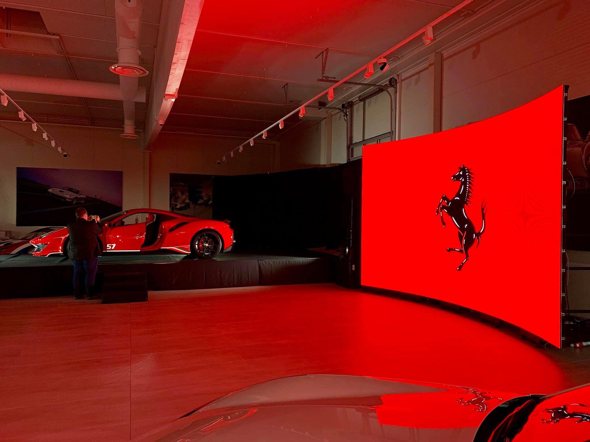 Punainen Ferrari-auto esillä Ferrari-logolla punaisella taustalla näyttelytilassa.