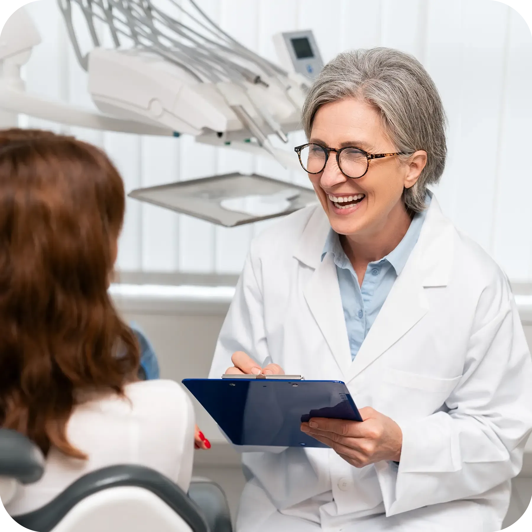 Smiling middle-aged female dentist looks at the patient and takes notes.